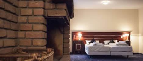 A hotel room with a brick fireplace, a bed with two pillows, a nightstand, and a lamp.