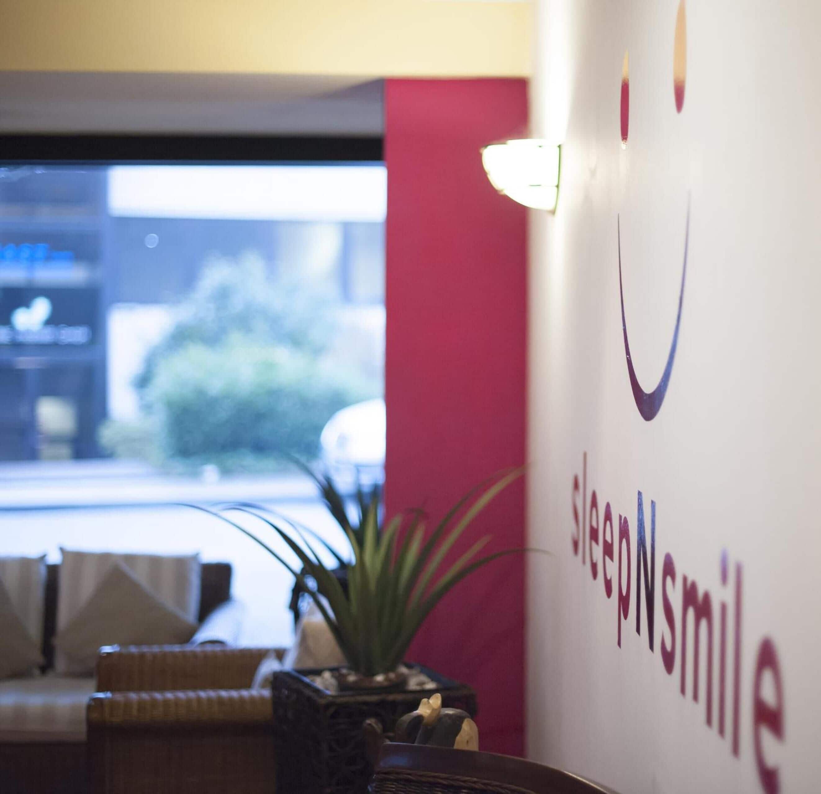 A reception area with a sign reading "sleepNSmile" and a plant in the foreground.