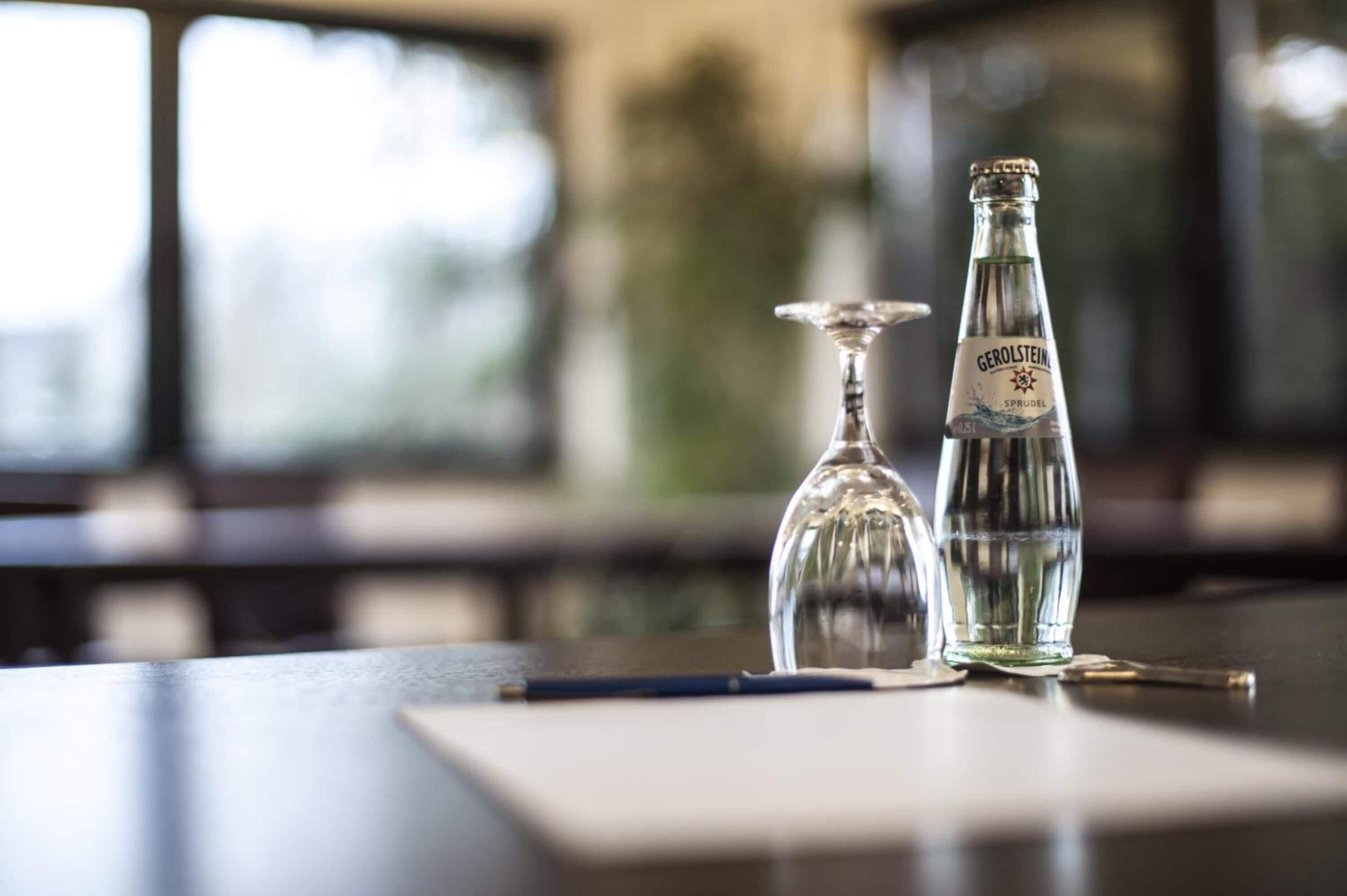 A bottle of Gerolsteiner beer and a glass on a table with a pen and a napkin.