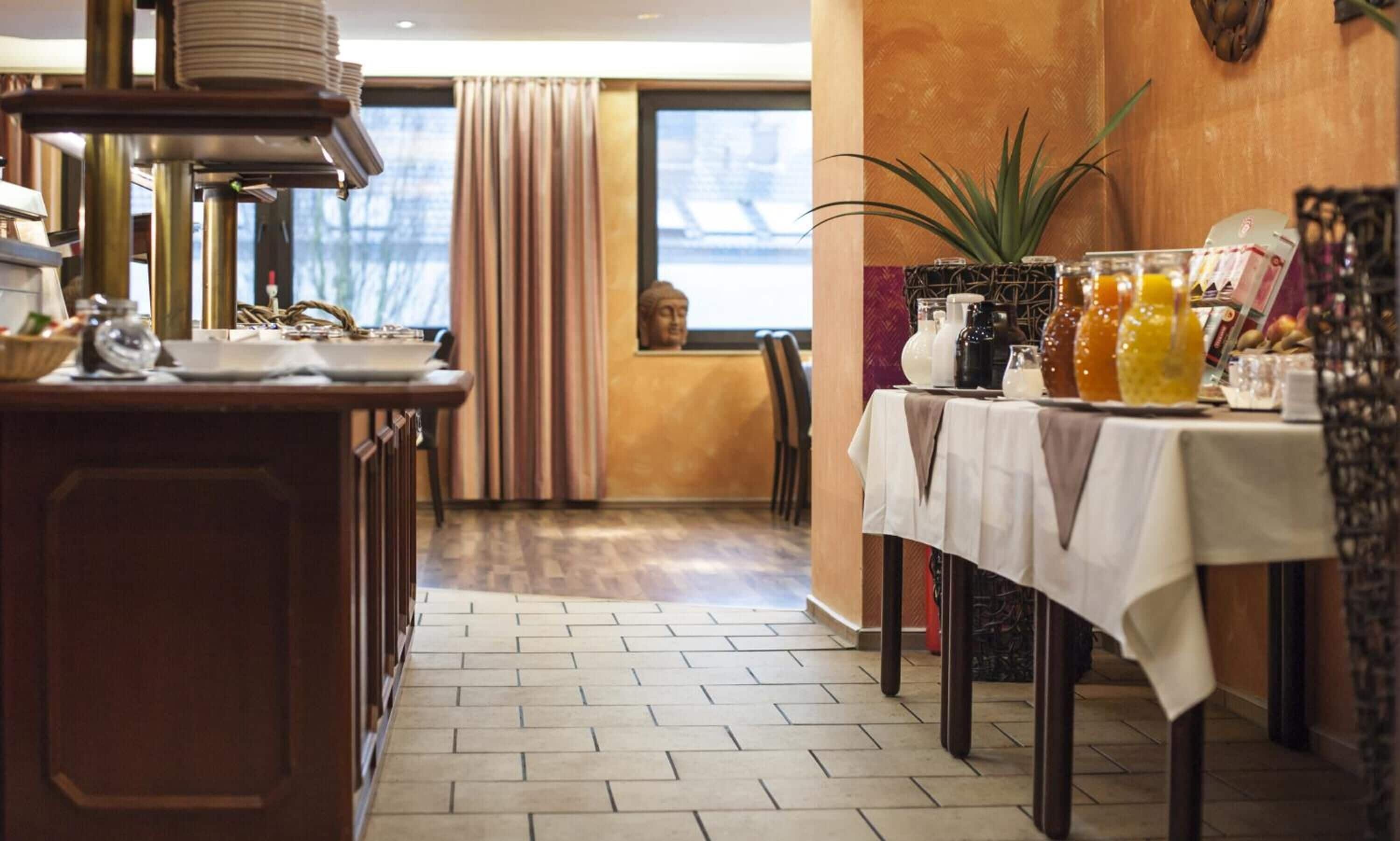 Et hotellets restaurantområde med buffet, en Buddha-figur og et bord med drikkevarer og tilbehør.