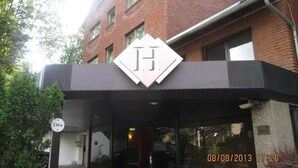 Entrada de hotel con un llamativo logotipo en forma de 'H', zona de acceso cubierta y un cartel de 2.00 metros.