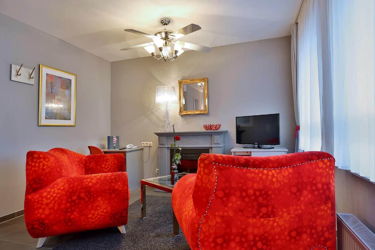 Un salon avec une cheminée, un téléviseur et deux fauteuils rouges.