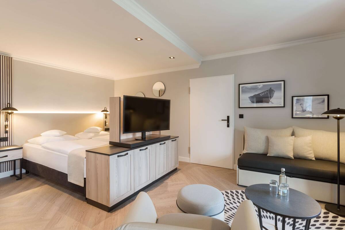 Une chambre d’hôtel moderne équipée d’un lit, d’une télévision, d’un canapé, d’un coin repas et ornée d’œuvres d’art sur les murs.
