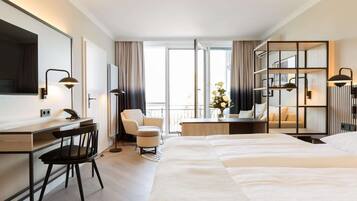 Ein Hotelzimmer mit einem großen Bett, einem Schreibtisch mit Stuhl, einer Couch und einem Balkon mit Blick.