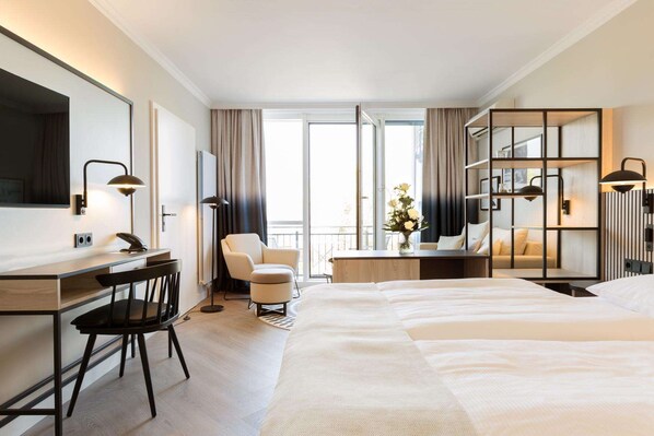 A hotel room with a large bed, a desk with a chair, a sofa, and a balcony with a view.