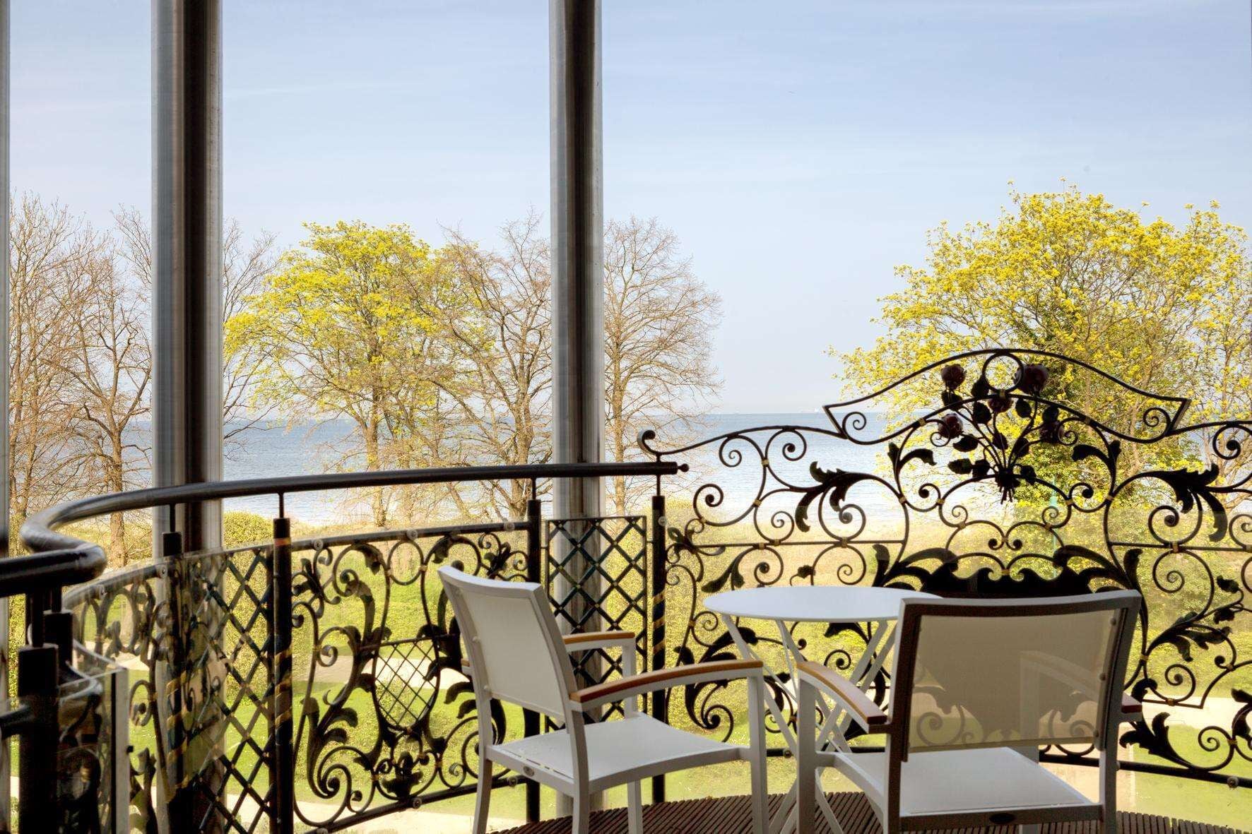 A balcony with a wrought iron railing, two white chairs, and a small table.