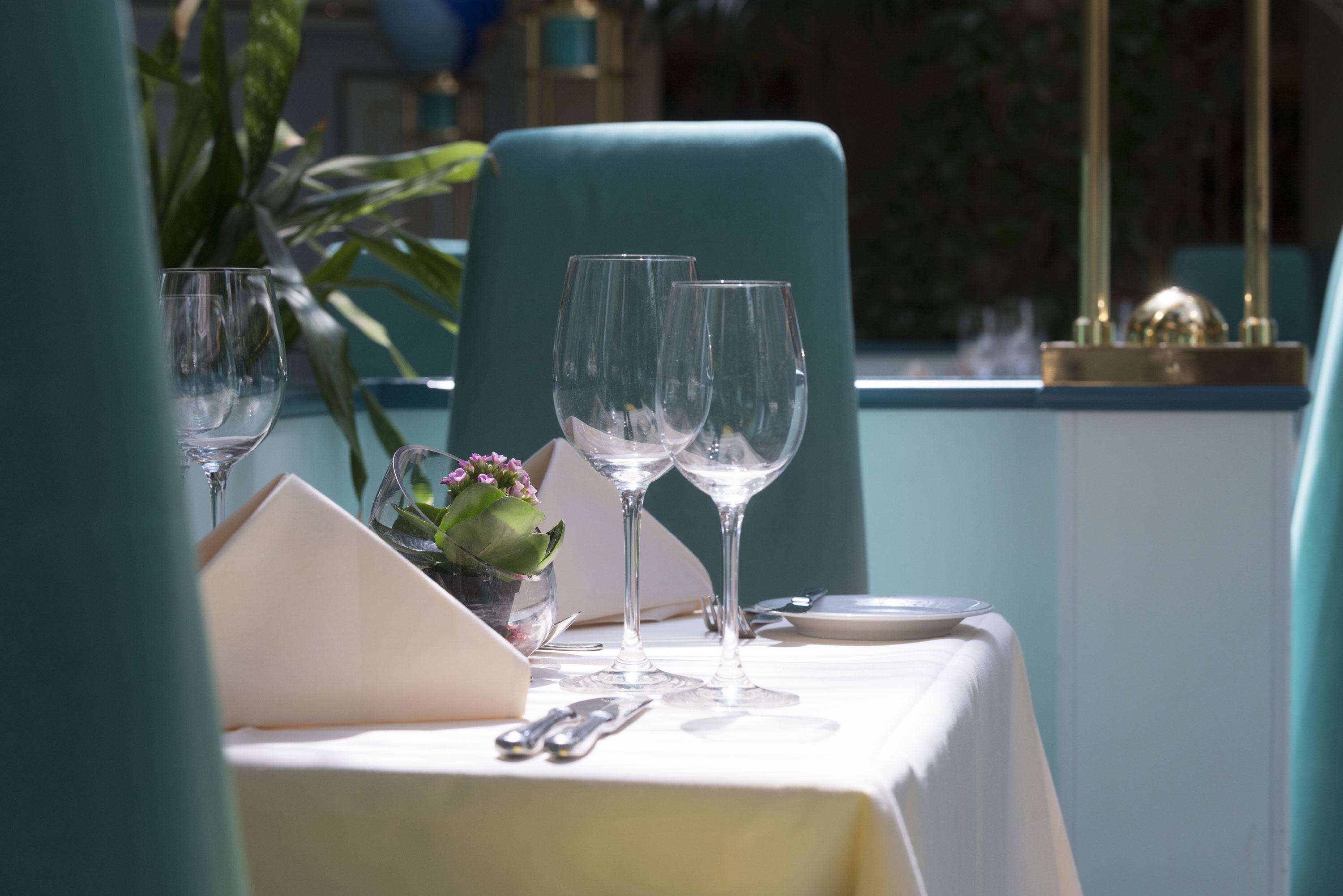 Una mesa servida con copas de vino, una pequeña planta en maceta y una servilleta.