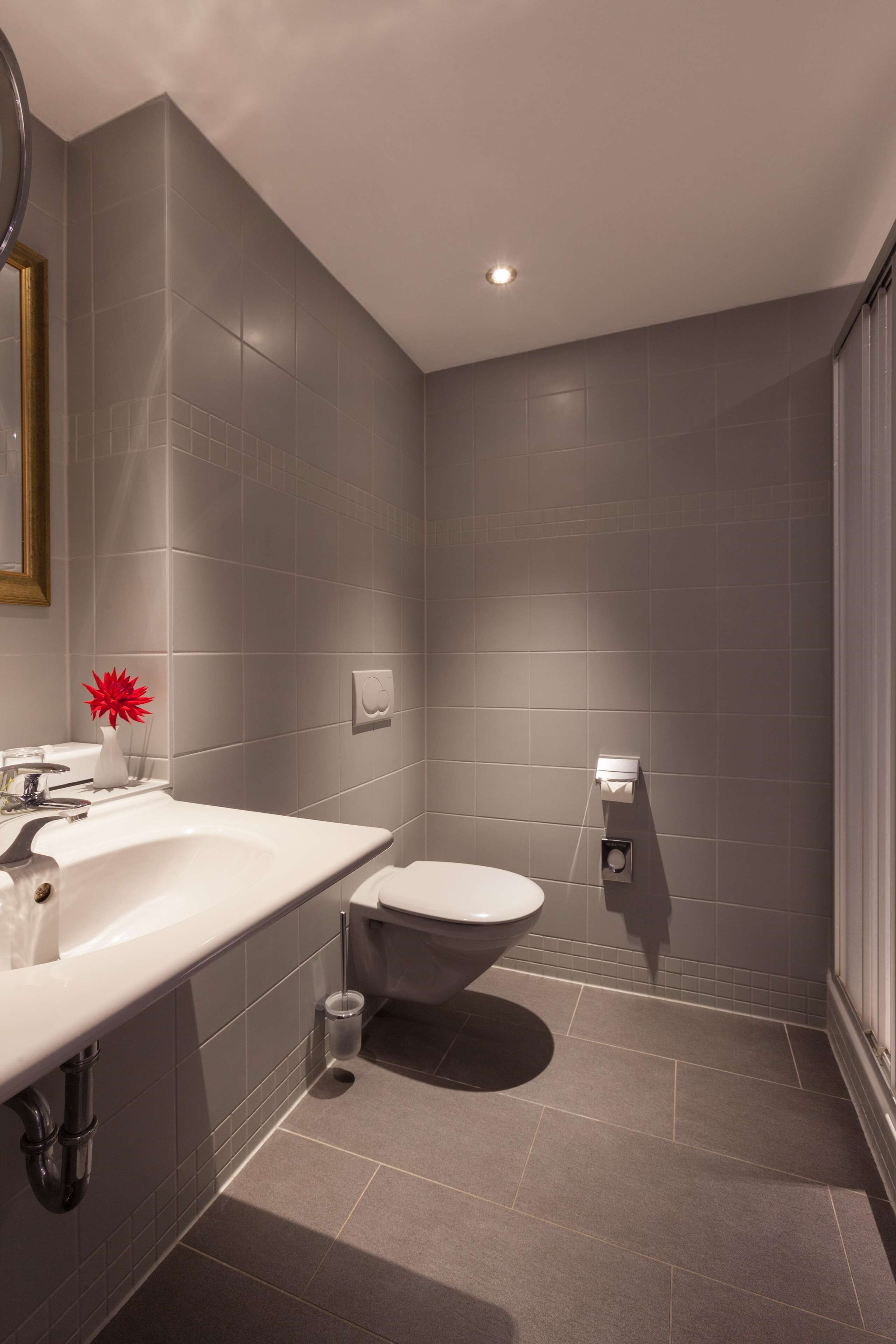 A modern bathroom with grey tiles, a white sink, a toilet, and a shower area.