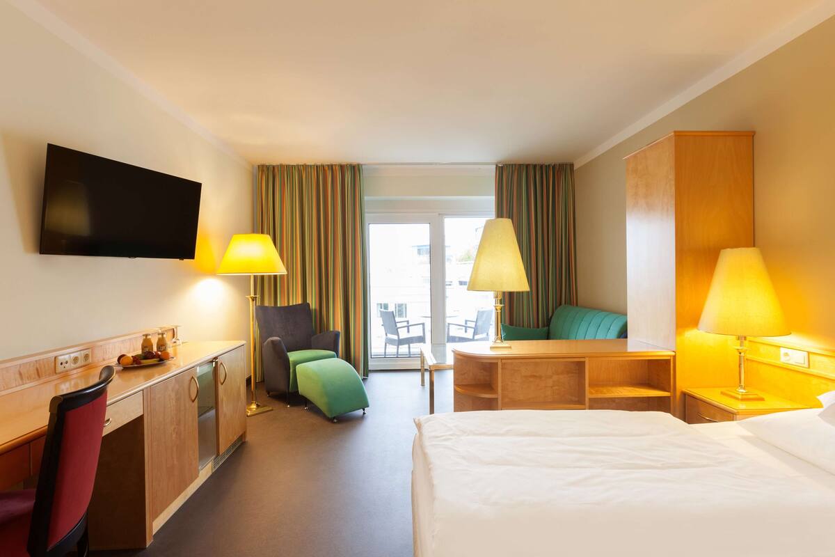 Une chambre d’hôtel avec un lit, un bureau, une chaise et un téléviseur fixé au mur.
