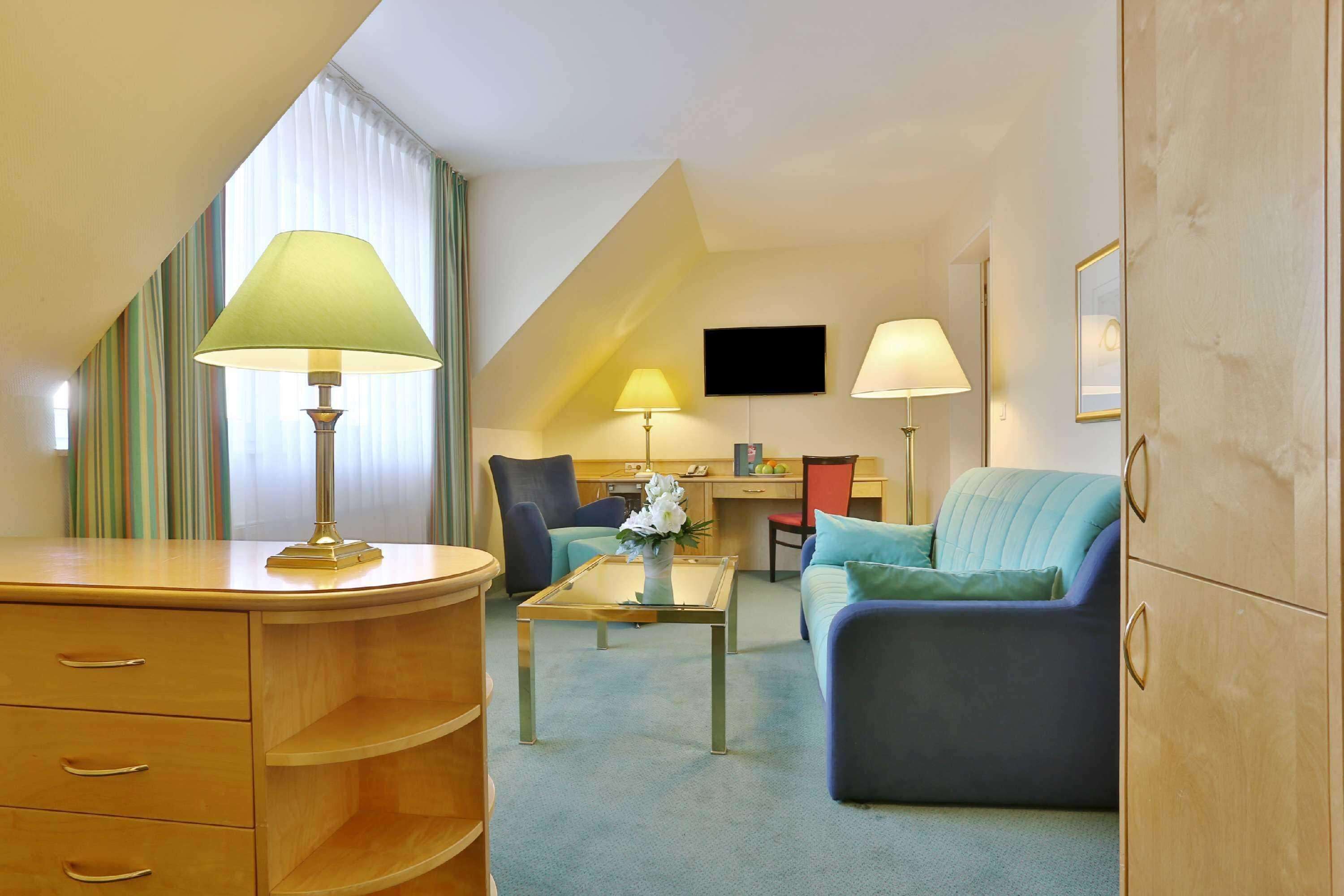 Una habitación de hotel con un escritorio, dos sillas, un sofá, una mesa de centro y dos lámparas.