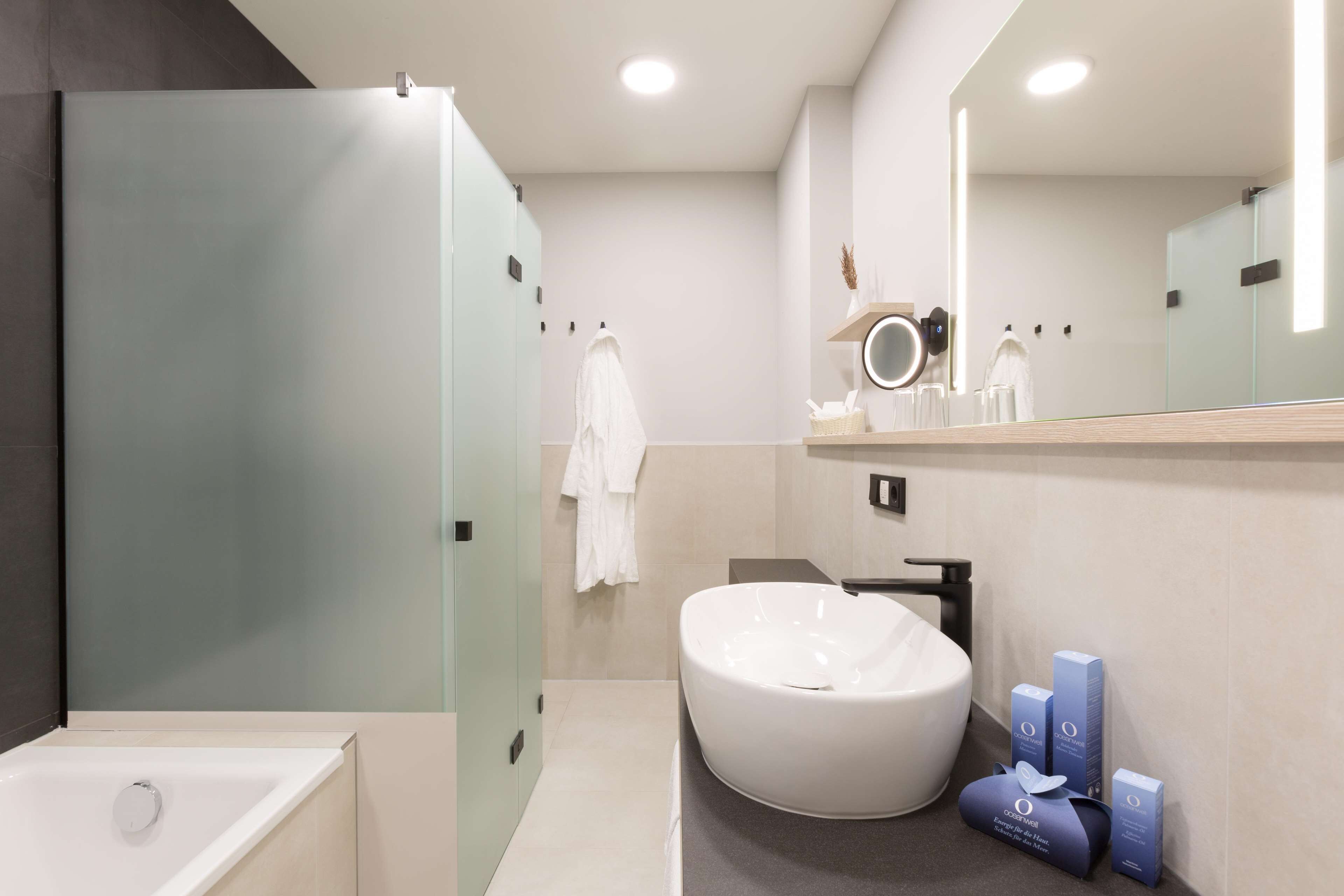 Un baño moderno con una bañera independiente, un lavabo grande y redondo, y un mueble de tocador con espejo y artículos de aseo.