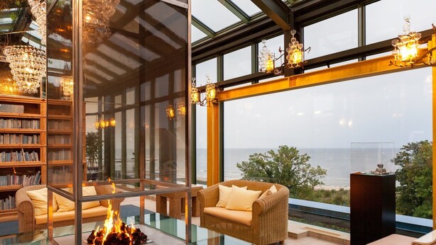 Un interior moderno con chimenea de vidrio, mobiliario de mimbre y vista al mar.
