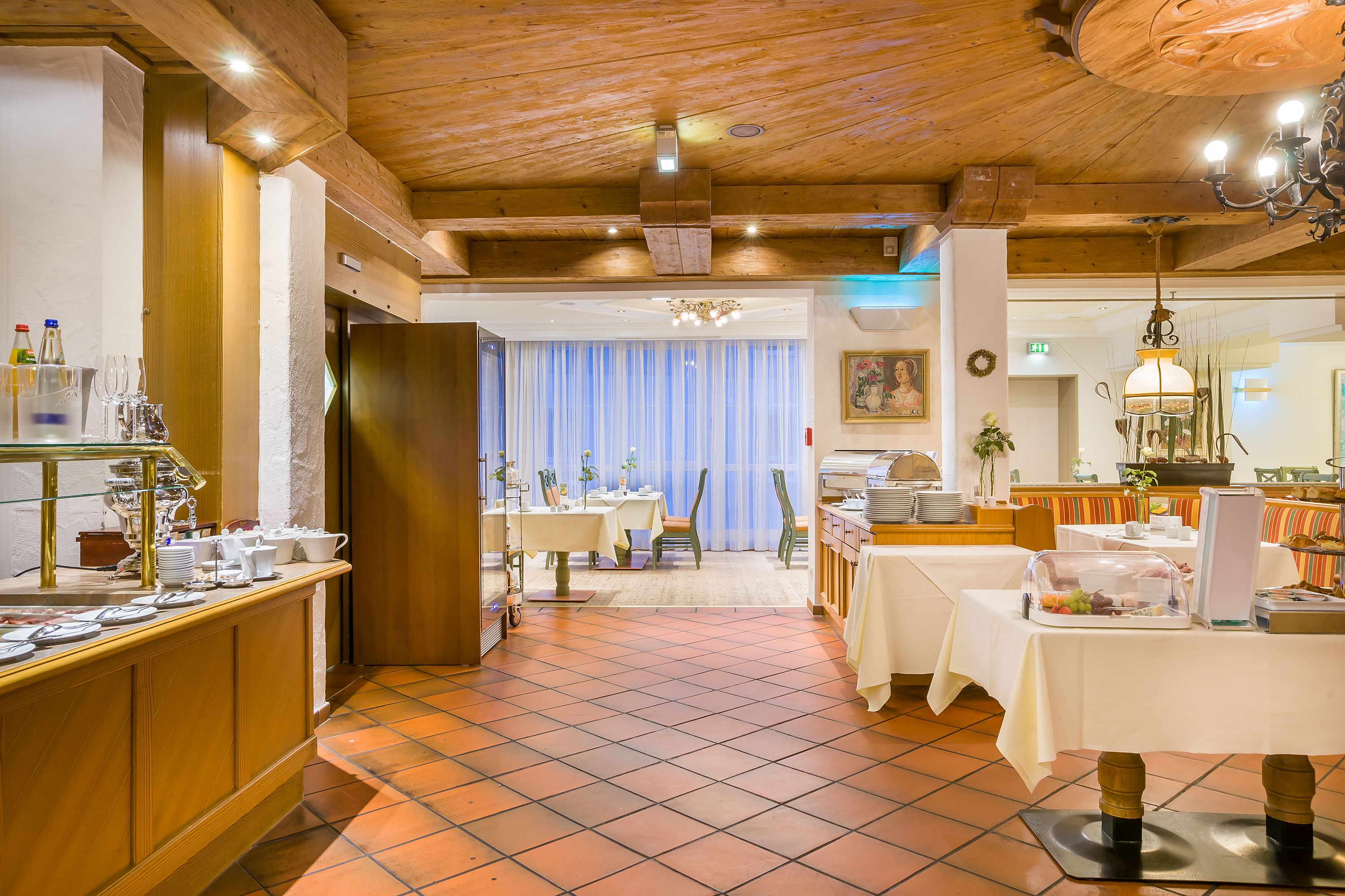 Ein Hotel-Essbereich mit Holzbalkendecke, gefliestem Boden und einem Buffet.