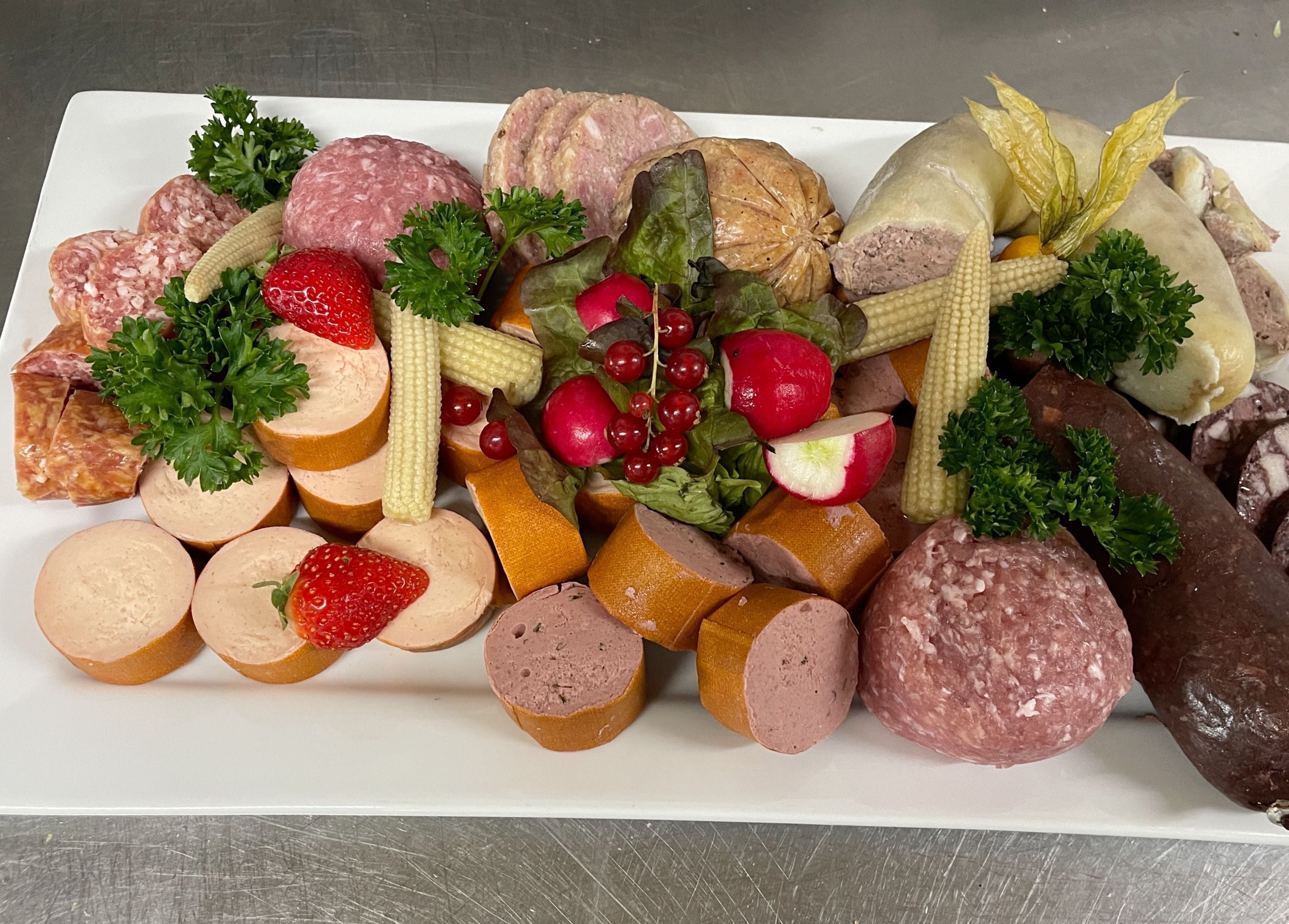A variety of sliced meats and vegetables on a white platter.