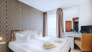 A hotel room with a large bed, a desk, a chair, and a television. - REGIOHOTEL Leipzig West (Schkeuditz)