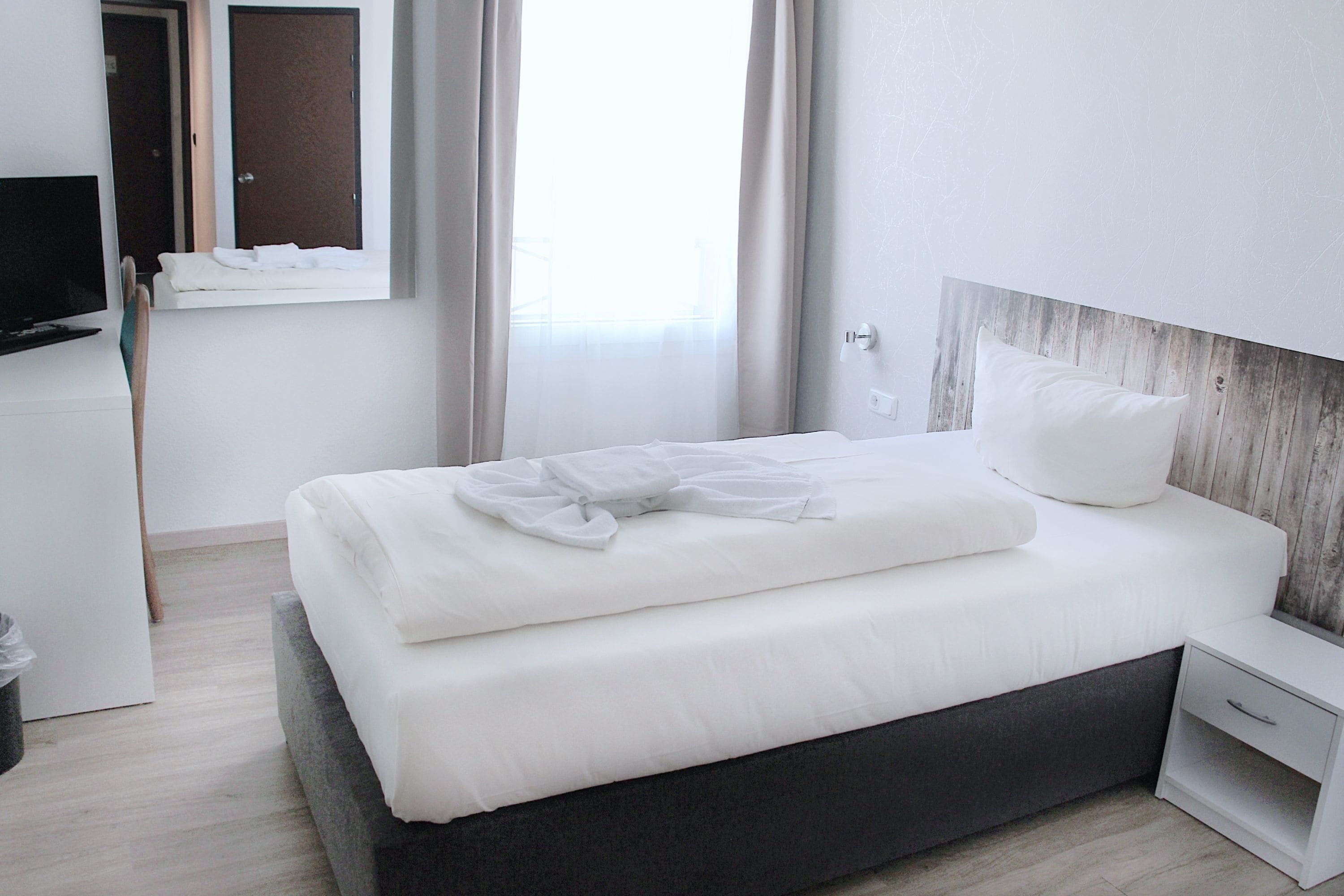 A modern hotel room with a bed, bedside table, and a TV on a stand.