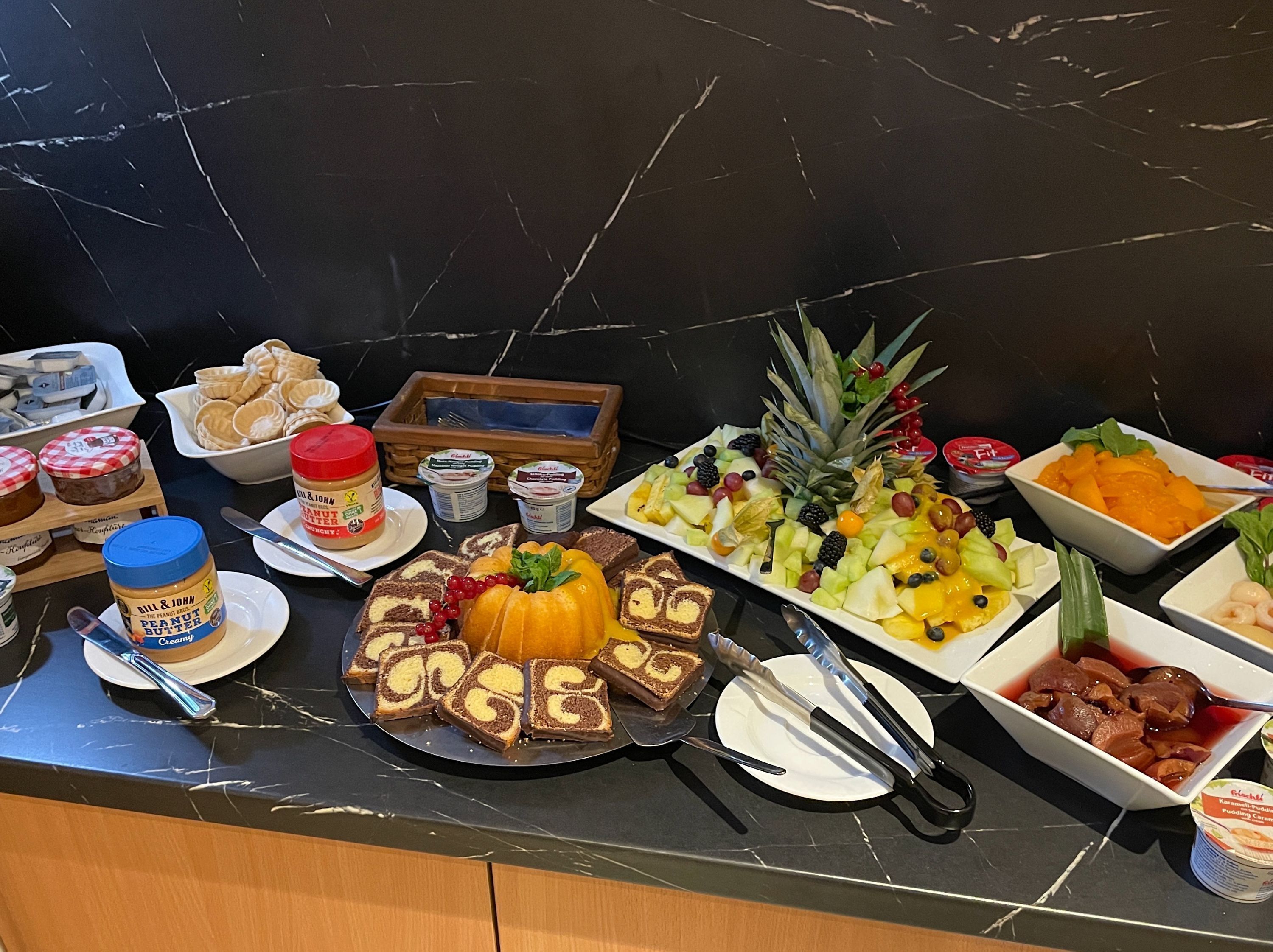 A buffet table with various food items including peanut butter, bread, fruits, and desserts.