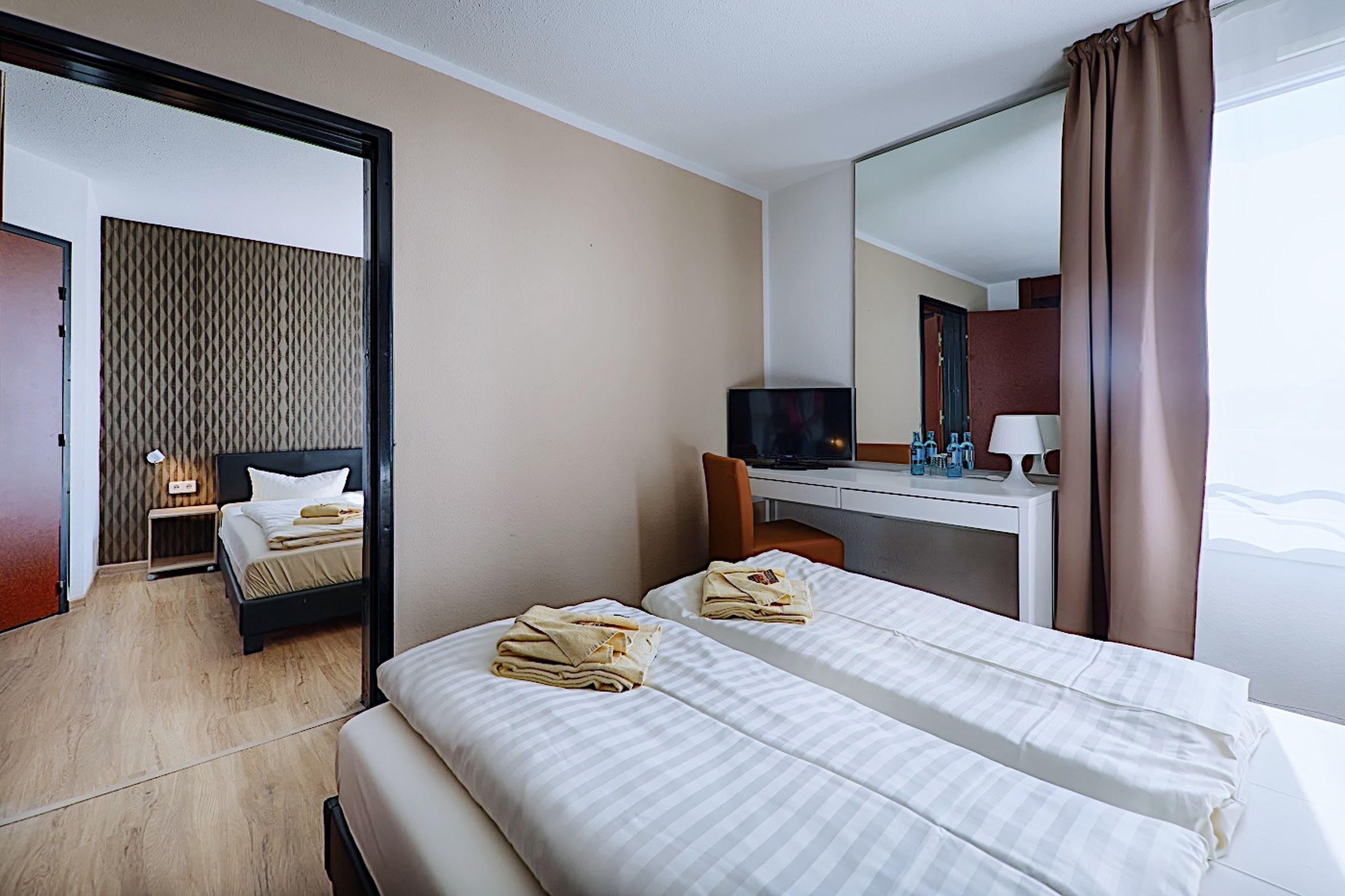 Habitación de hotel con dos camas, un escritorio con computadora, televisor y espejo.