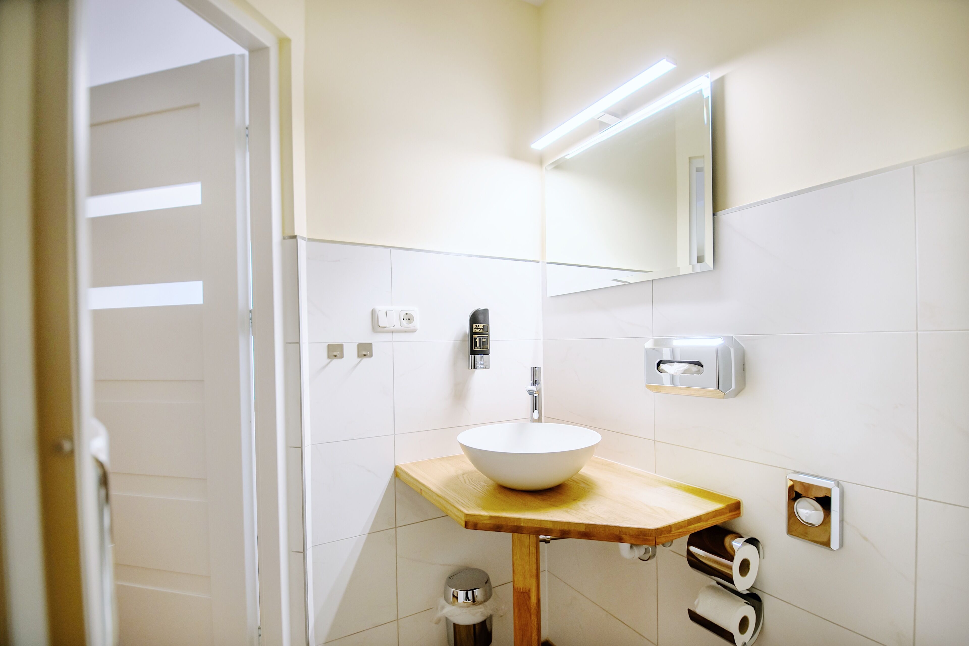 A bathroom with a white sink, wooden countertop, mirror, and toilet paper dispenser.