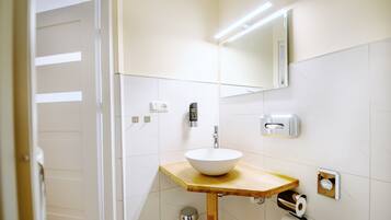 A bathroom with a white sink, wooden countertop, mirror, and toilet paper dispenser.