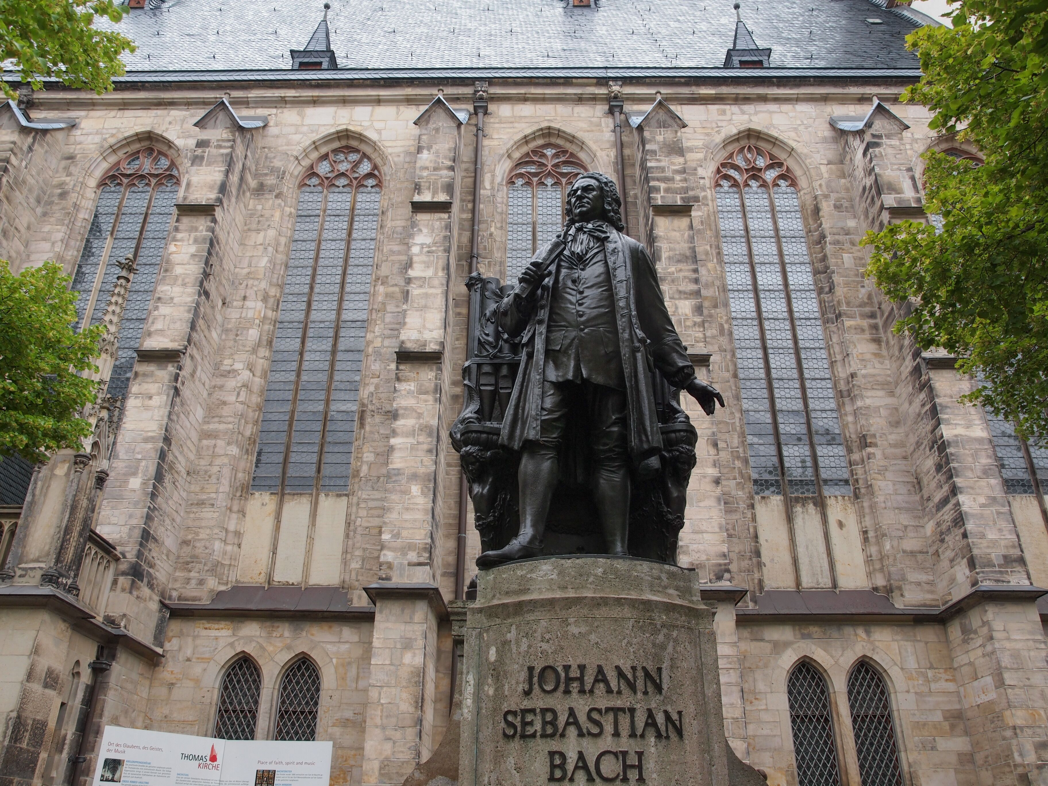 Una estatua de Johann Sebastian Bach frente a un edificio histórico con ventanas arqueadas y tejado de tejas.