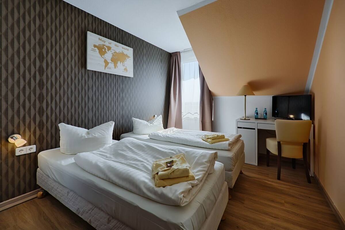 A hotel room with two beds, a desk, a chair, and a TV.