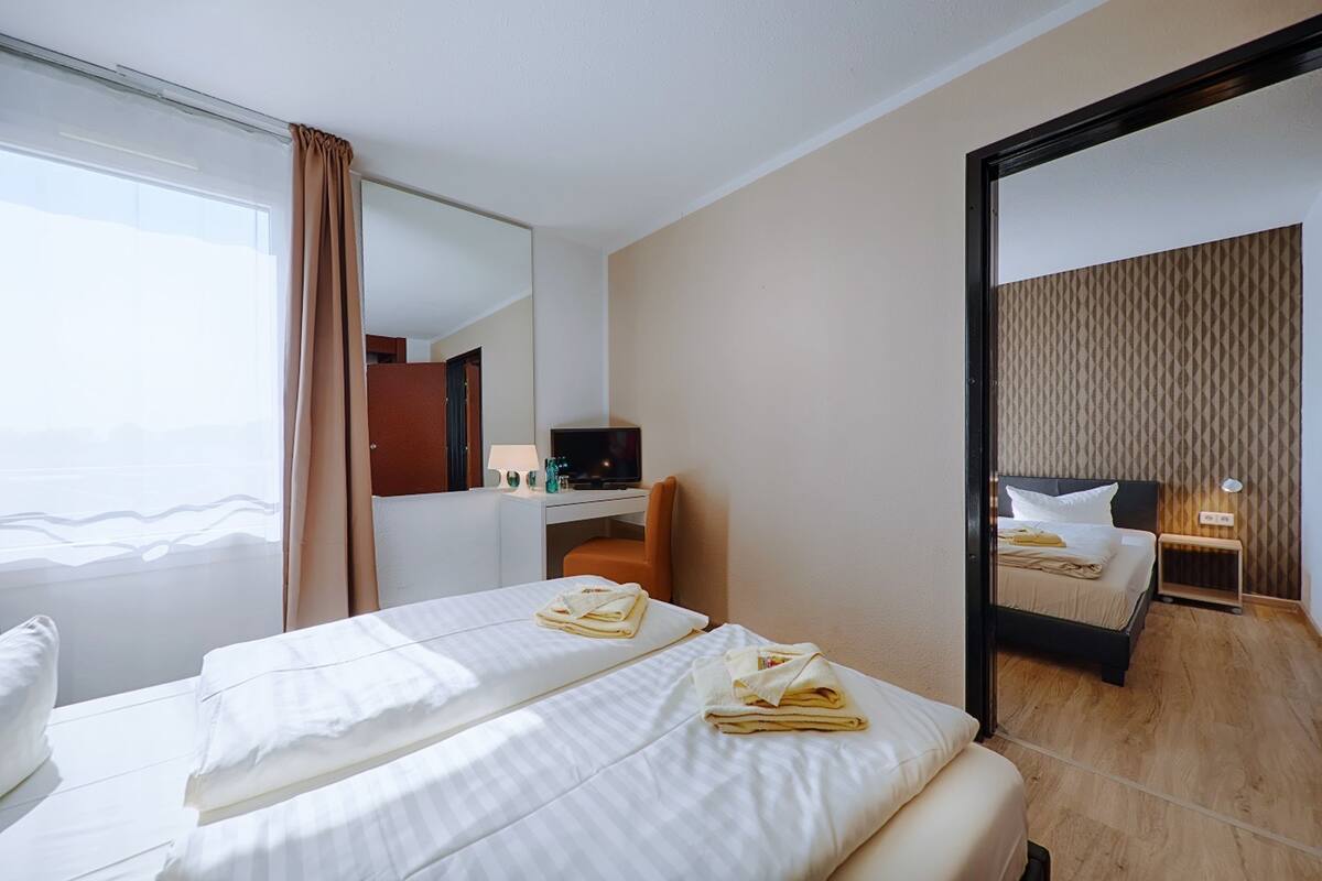 A hotel room with two beds, a desk, a TV, and a large mirror.