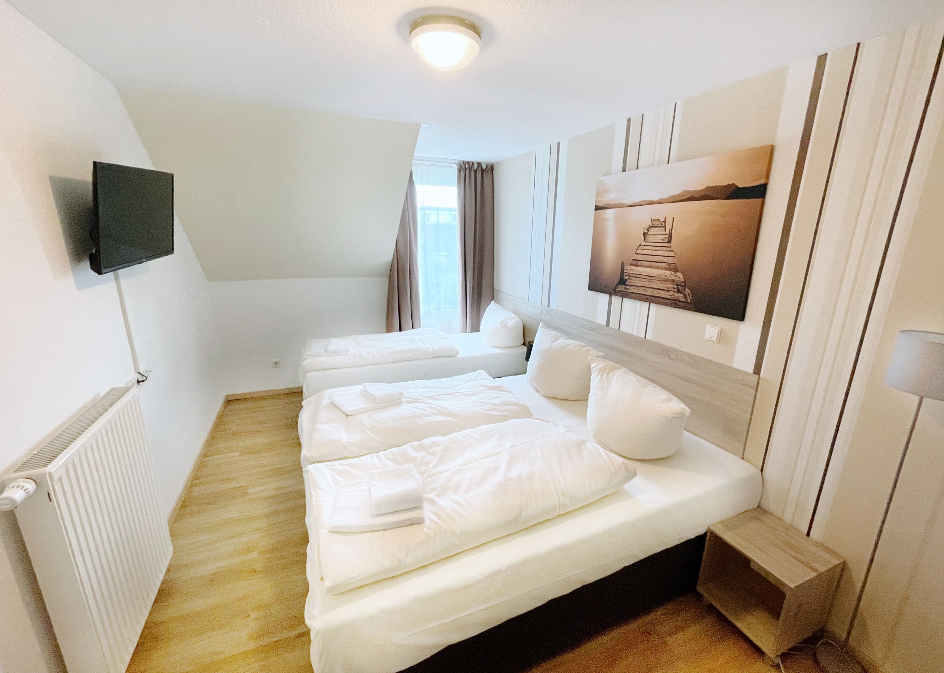 Habitación de hotel con dos camas, un televisor de pantalla plana montado en la pared, un radiador y un cuadro de una escalera de madera.