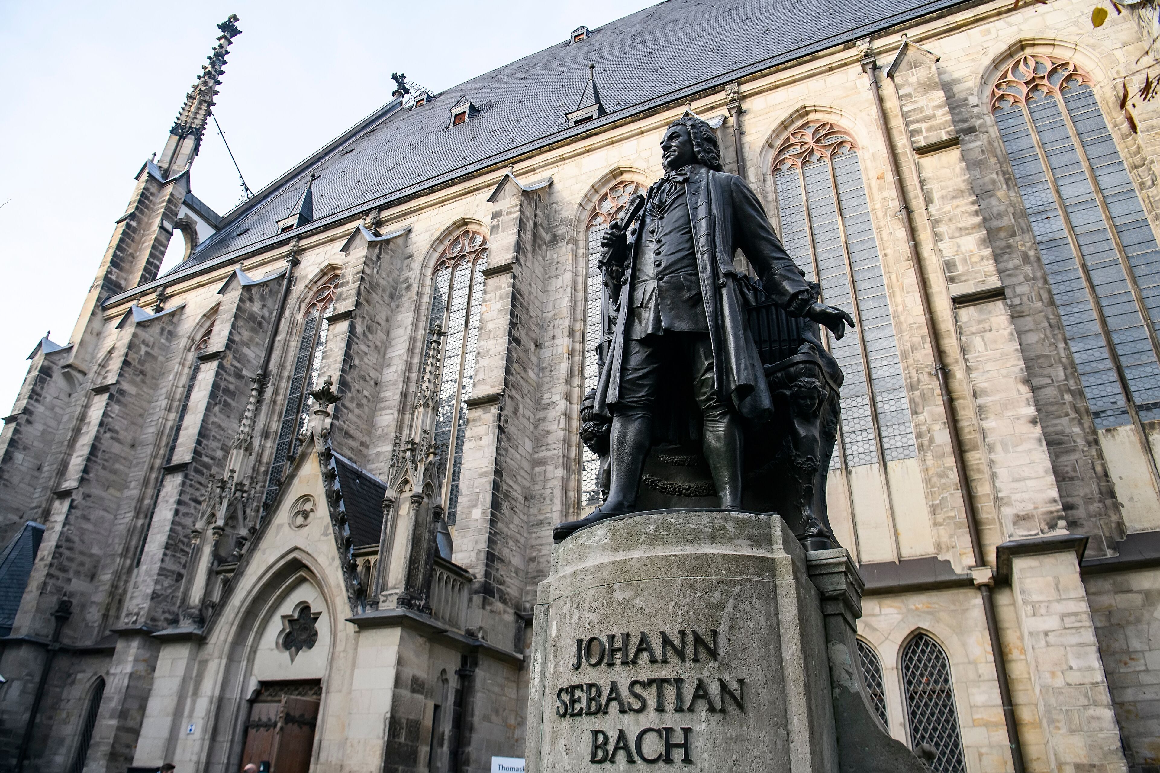 Une statue de Jean-Sébastien Bach se dresse devant un bâtiment historique à l’architecture gothique.