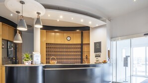 A modern reception area with a curved black counter, wooden cabinets, and a clock on the wall. - Hotel Belmondo Leipzig Airport by Mayburgh (Wiedemar)