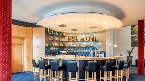 A bar area with a curved ceiling, bar stools, and a variety of bottles and glasses on shelves. - Hotel Belmondo Leipzig Airport by Mayburgh (Wiedemar)