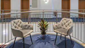 A balcony with two upholstered chairs and a potted plant, surrounded by a metal railing. - Hotel Belmondo Leipzig Airport by Mayburgh (Wiedemar)