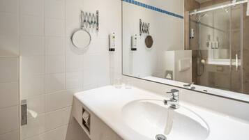 Un baño moderno con un lavamanos grande, un espejo y una ducha con cerramiento de vidrio.