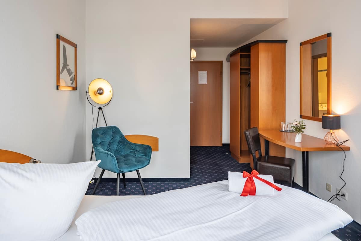 A hotel room with a bed, a desk, a chair, a lamp, and a mirror.