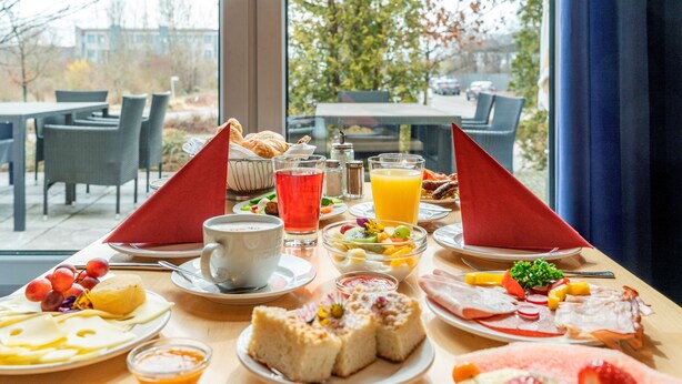 A breakfast buffet with various dishes, including pastries, fruits, and beverages, set on a table with a view of the outdoors. - Hotel Belmondo Leipzig Airport by Mayburgh (Wiedemar)
