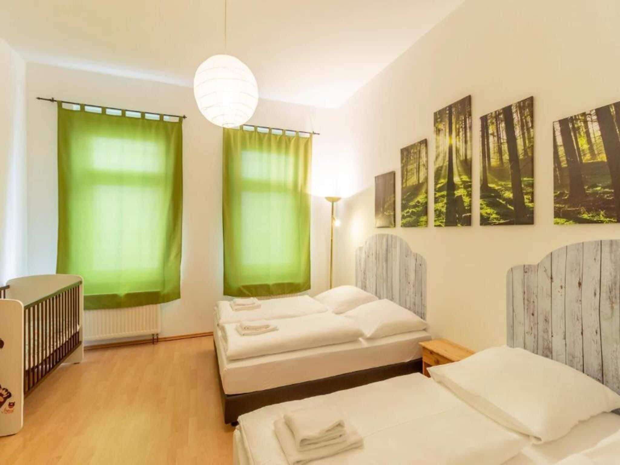 A hotel room with two beds, a radiator, a crib, and forest-themed wall art.