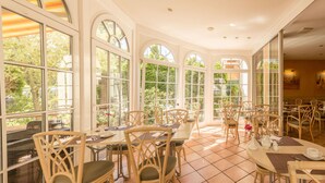 Une salle à manger spacieuse, dotée de grandes fenêtres, de chaises en osier et d’un sol carrelé.
