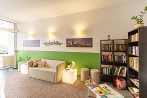 A modern living room with a sofa, a coffee table, a bookshelf, and a small table with children's books. - Hotel Markgraf Leipzig (Leipzig)