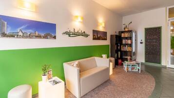 Un área de recepción con un sofá, una estantería y una pared verde decorada con imágenes de la ciudad.