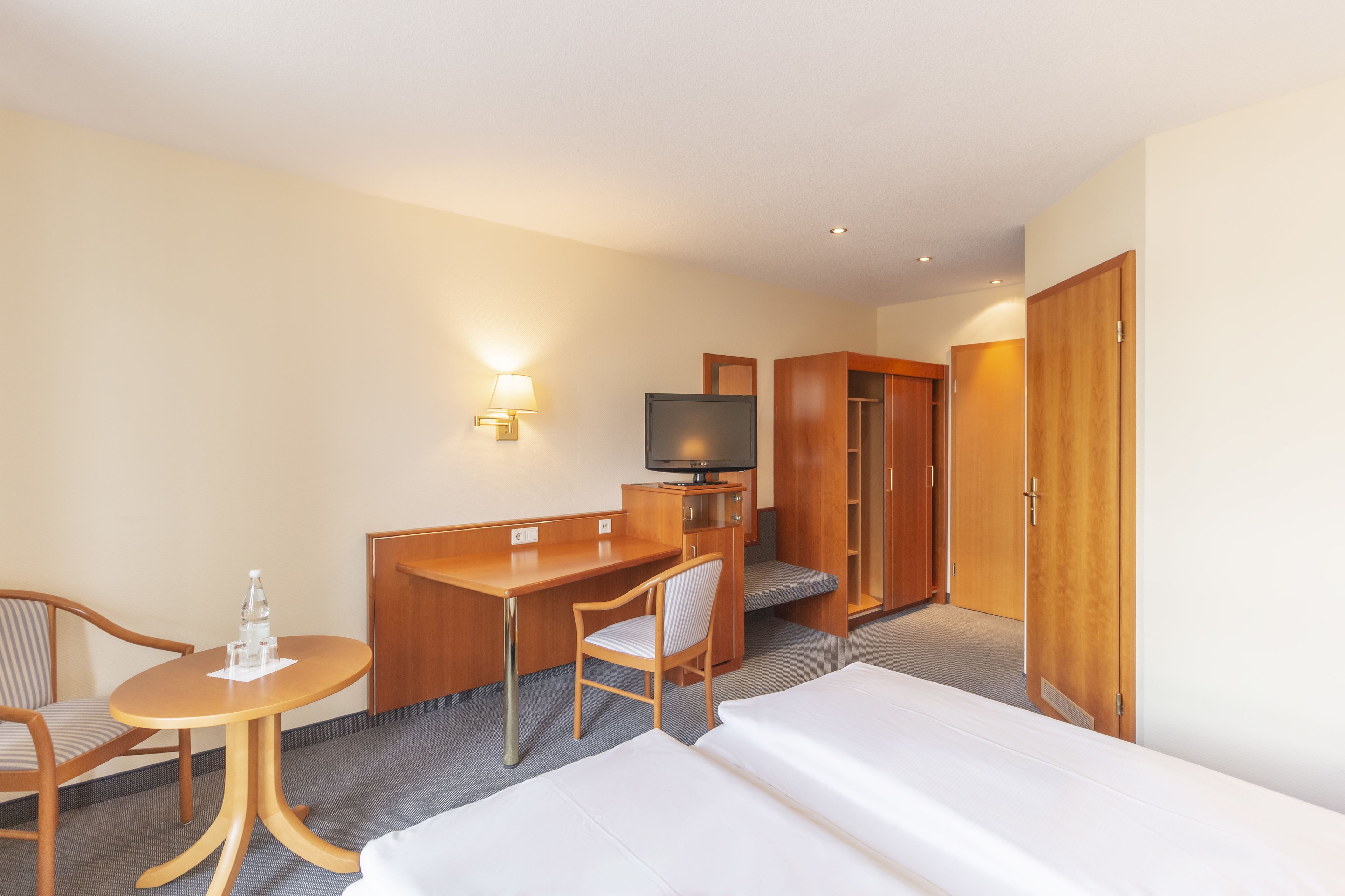 Habitación de hotel con cama, escritorio, silla, televisor y armario.