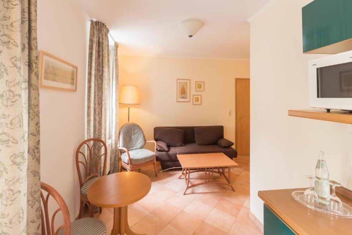 Una sala de estar con sofá, mesa de comedor, sillas, lámpara y televisor.