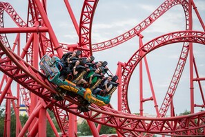 Una montaña rusa con pasajeros en primer plano y una estructura metálica roja al fondo.