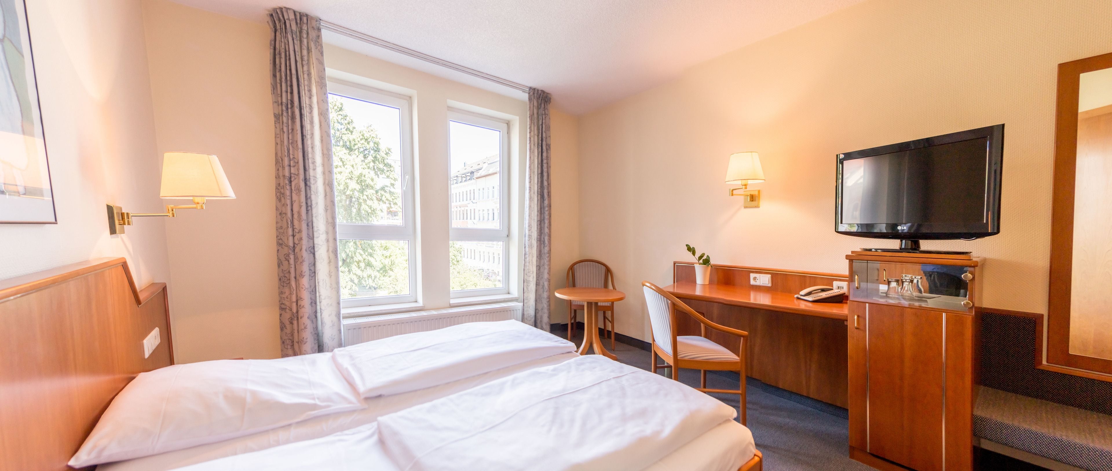 A hotel room with a bed, a desk, a chair, a television, and a window with curtains.