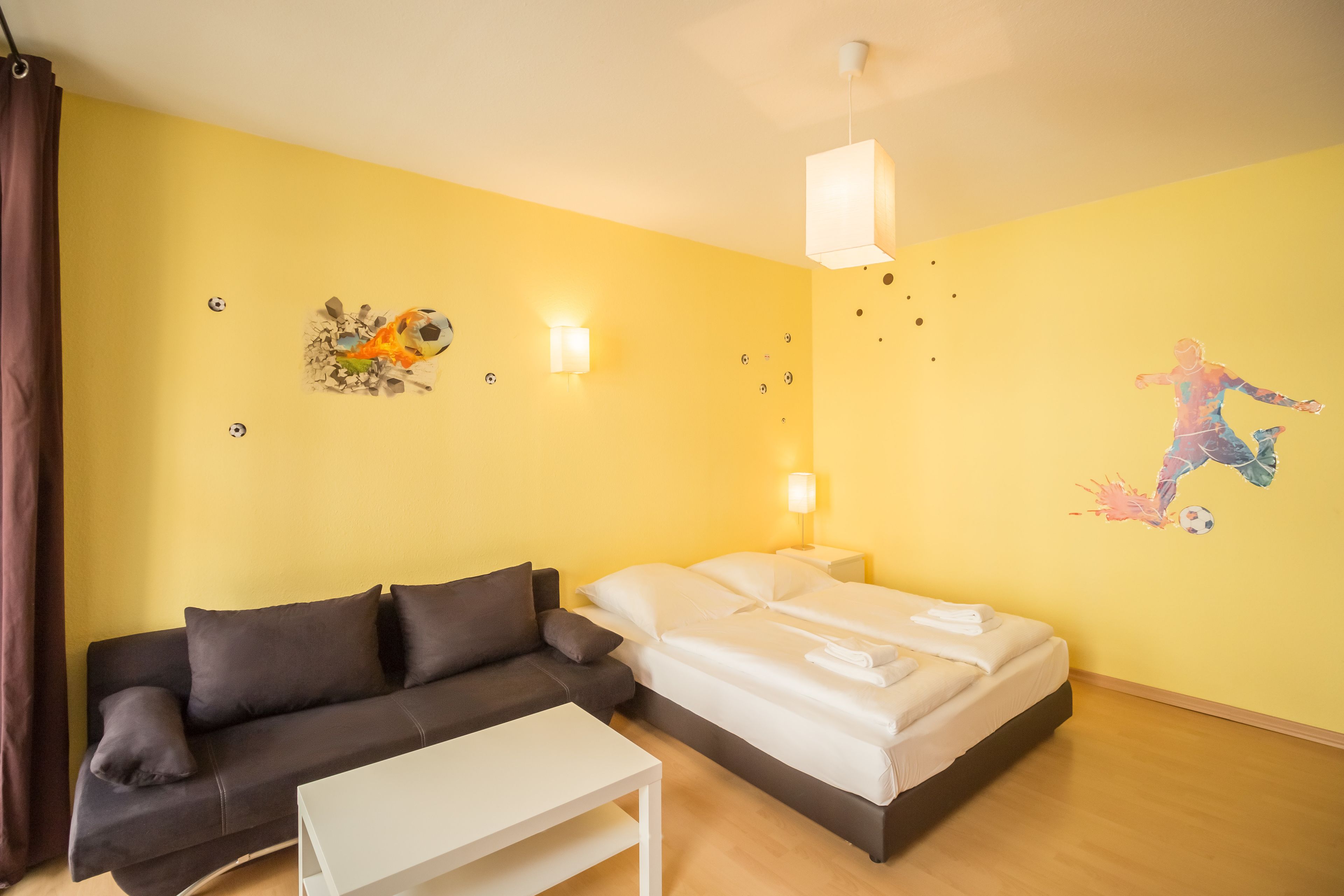 Une pièce comprenant un lit, un canapé, une petite table et des éléments de décoration murale, notamment un ballon de football et une fresque.