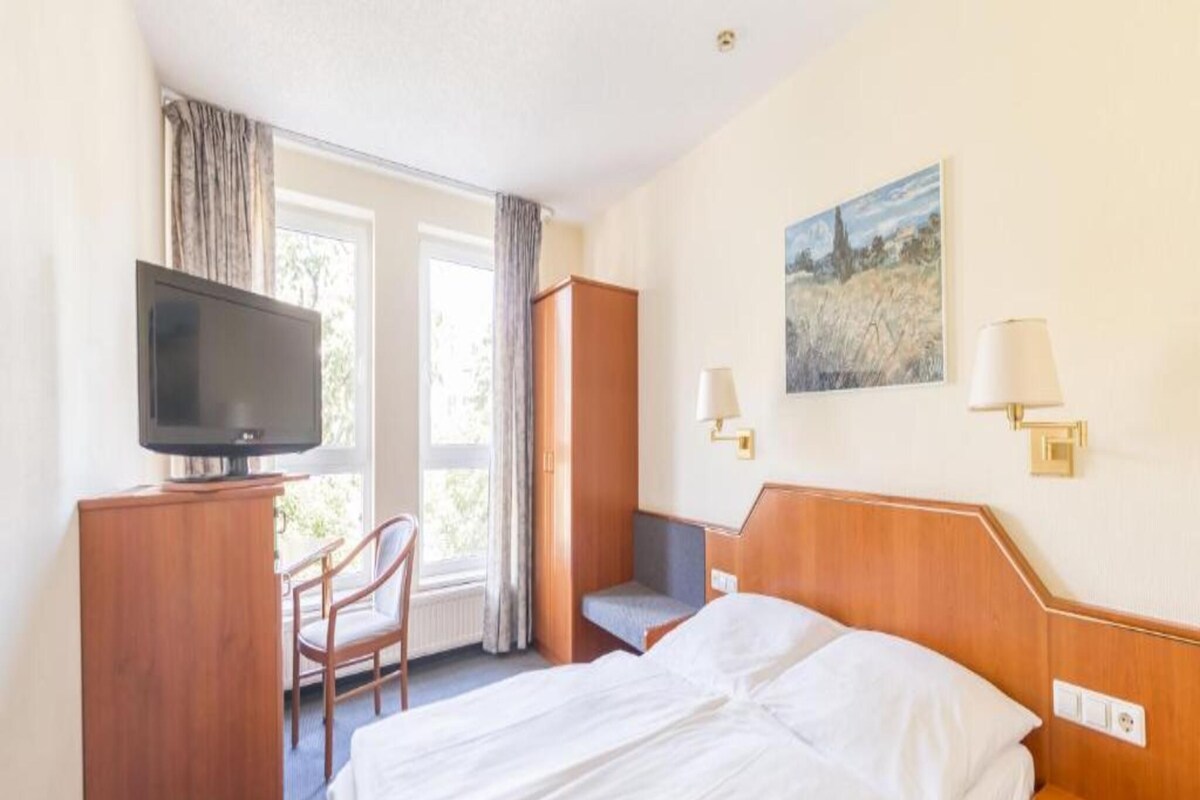 Habitación de hotel con cama, escritorio con televisor, silla, armario y un cuadro en la pared.