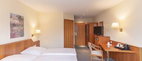 A hotel room with a bed, a desk, a chair, a television, and a painting on the wall.