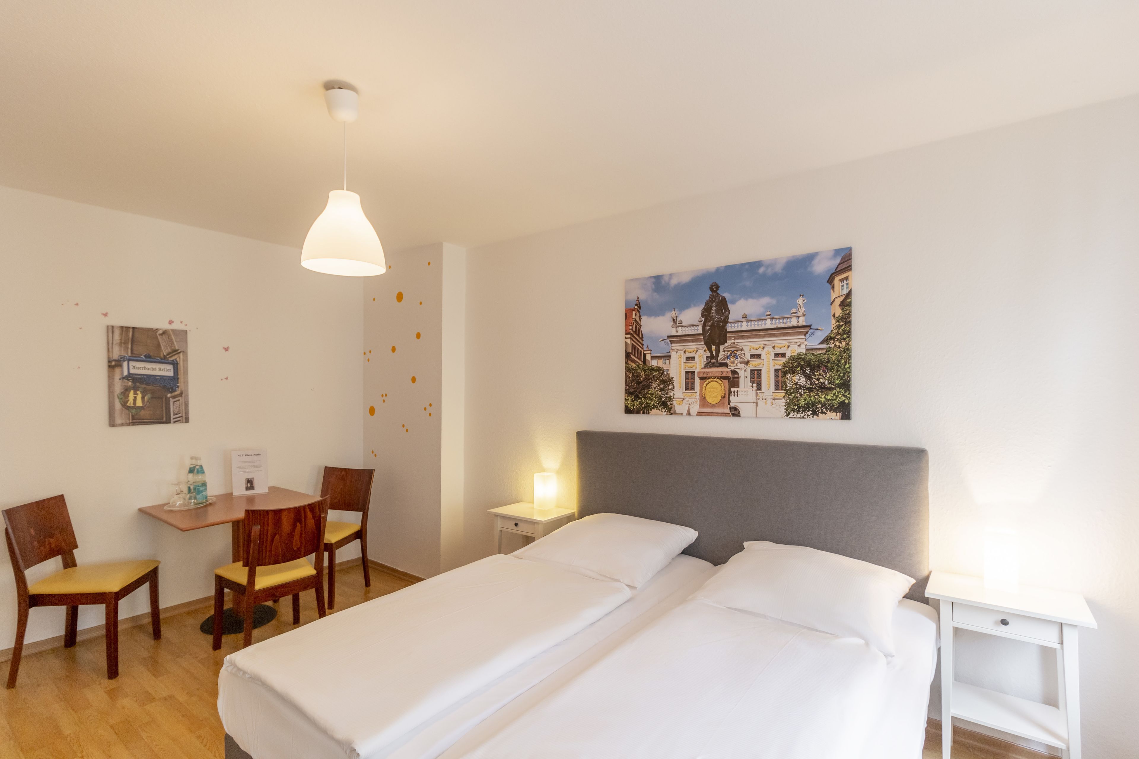A hotel room with a bed, a desk, two chairs, a small table, and a nightstand.