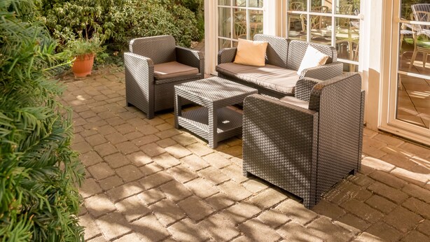 Un espace patio aménagé avec des meubles en osier, notamment un canapé et deux fauteuils, ainsi qu’une plante en pot.