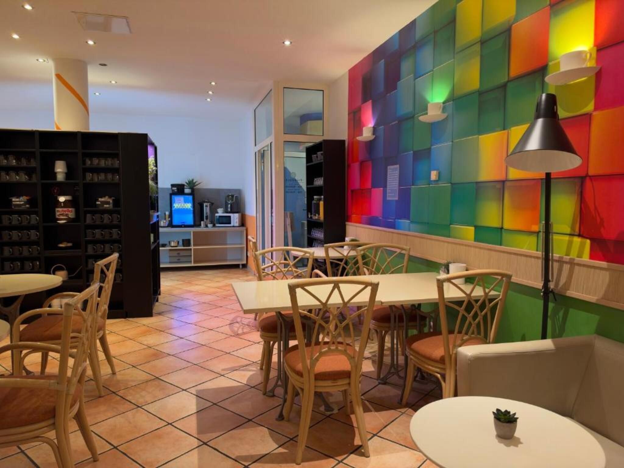 Un restaurante con una pared colorida, sillas de madera y piso de baldosas.
