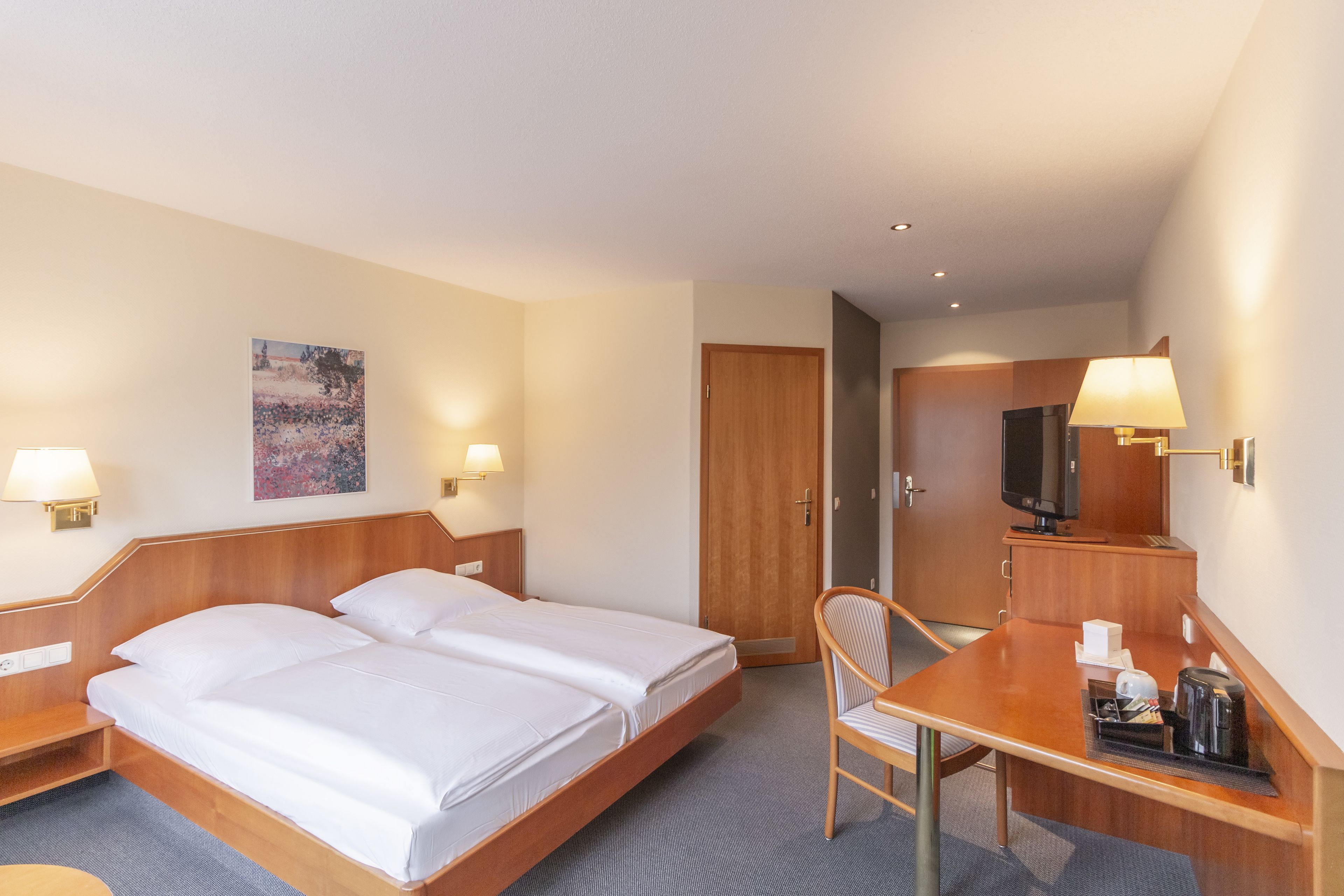 A hotel room with a double bed, a desk with a chair, a television, and a painting on the wall.